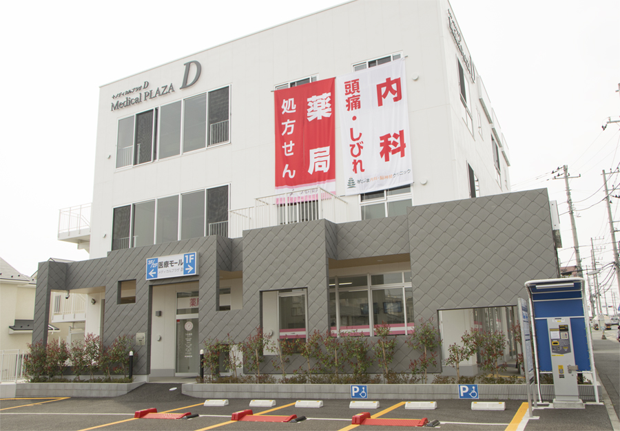 クリニックは白い建物です。Medica PLAZA Dという目印があります